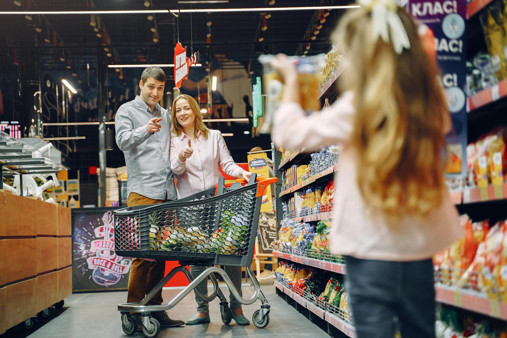 Happy family shopping in supermarket aisle with daughter holding snack box.