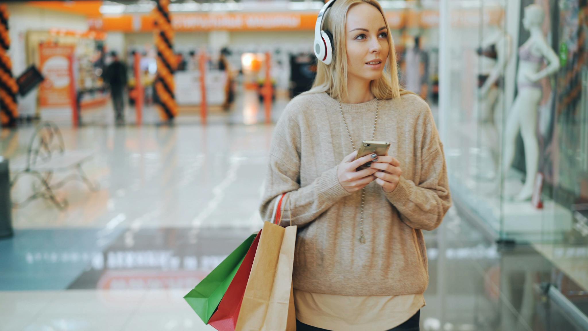 Woman shopping with bags and headphones in a busy mall.
